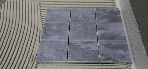 Graue Mosaikfliese auf Untegrund mit Fliesenkleber